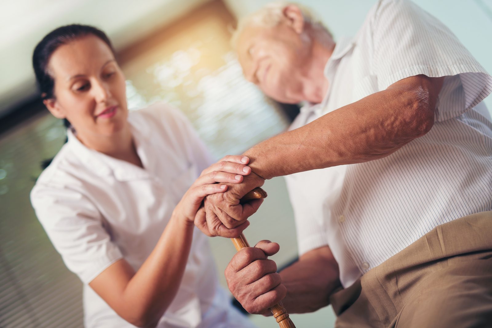 Carer supporting an older man with a walking stick during stroke recovery
